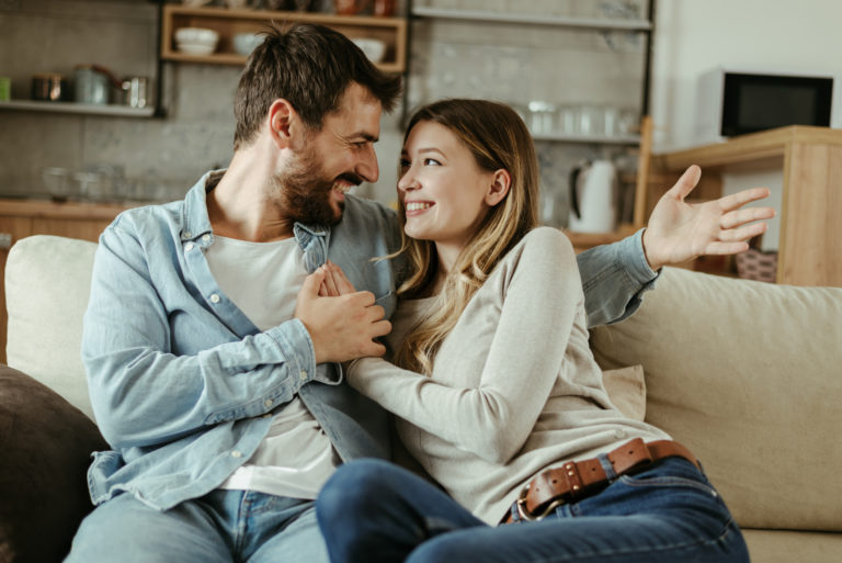 un homme et une femme souriants sont assis enlacés sur le canapé