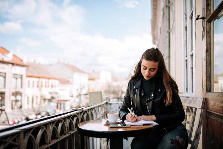 une belle femme est assise à une table extérieure et écrit une lettre