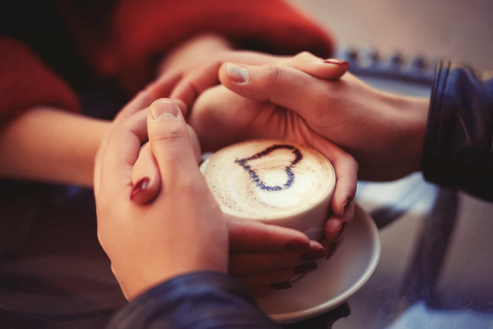 couple main dans la main avec une tasse de café entre