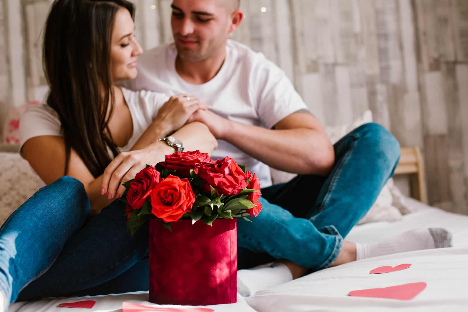 un homme et une femme assis sur un lit avec un bouquet de roses