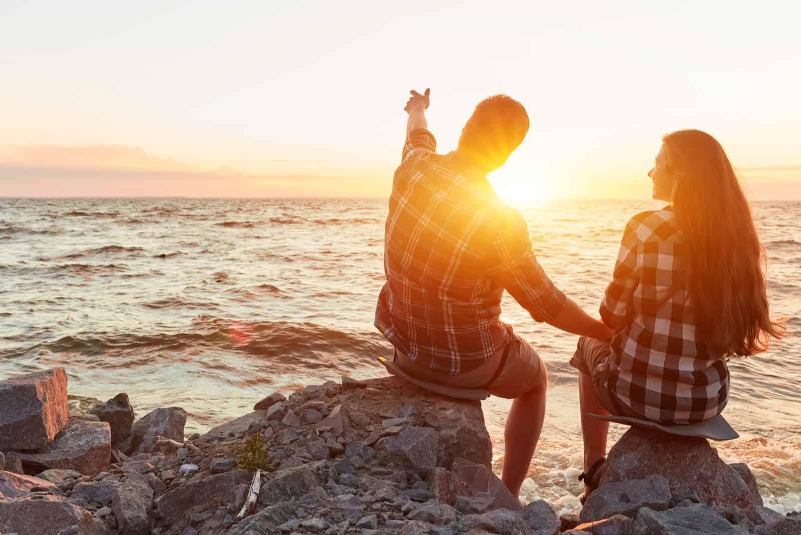 un homme et une femme assis sur un rocher regardant le coucher du soleil