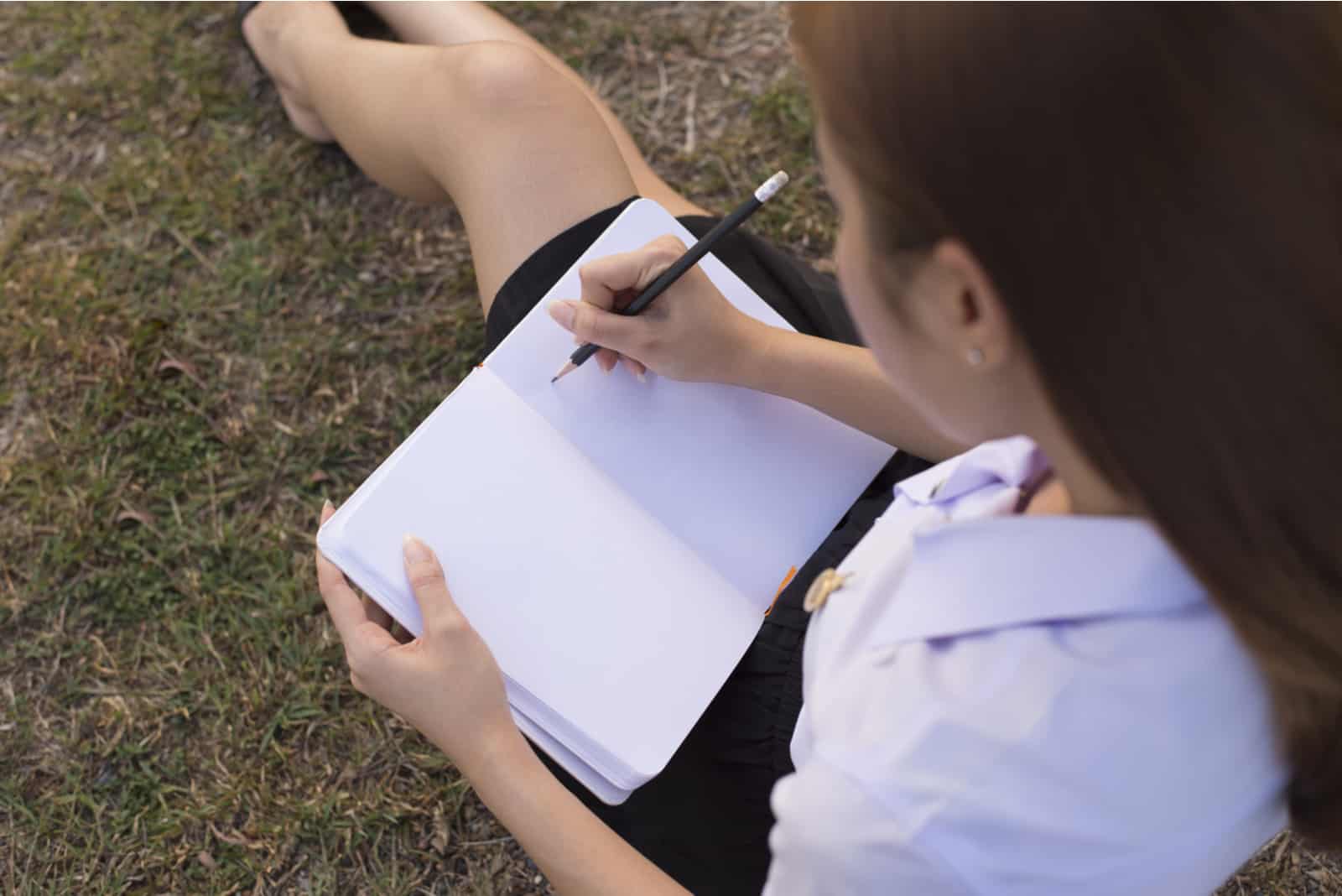 une femme assise sur l'herbe et écrivant