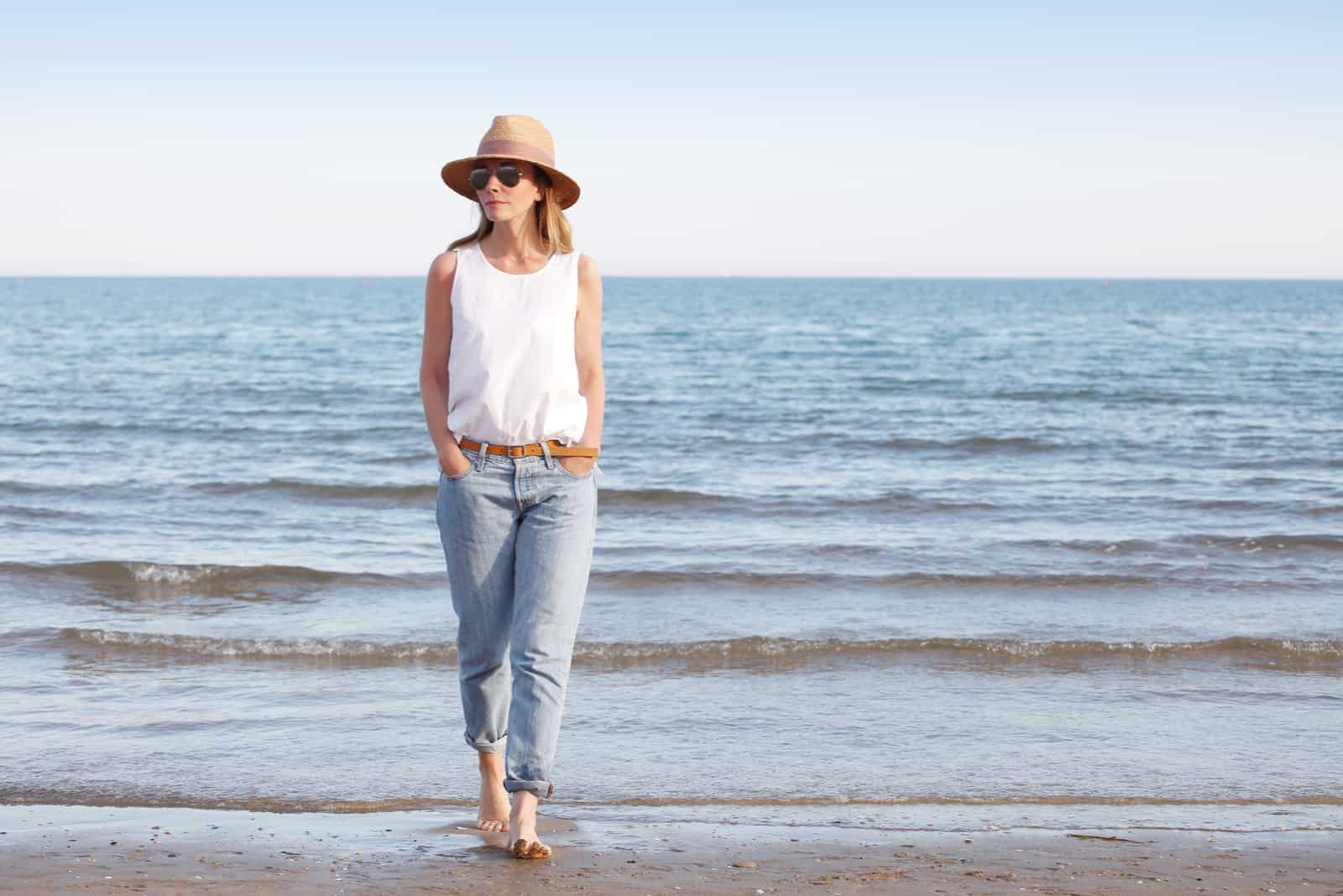 une femme avec un chapeau sur la tête marche sur la plage