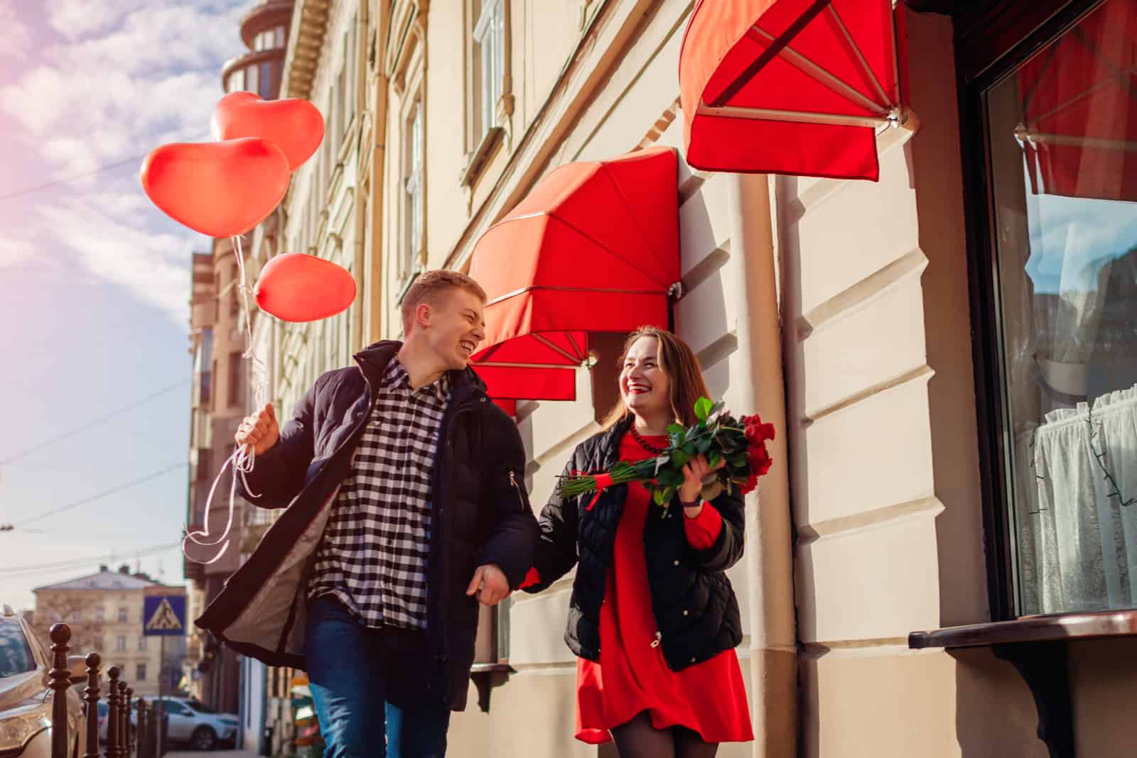 une femme souriante marche dans la rue avec un bouquet de roses et tient la main d'un homme