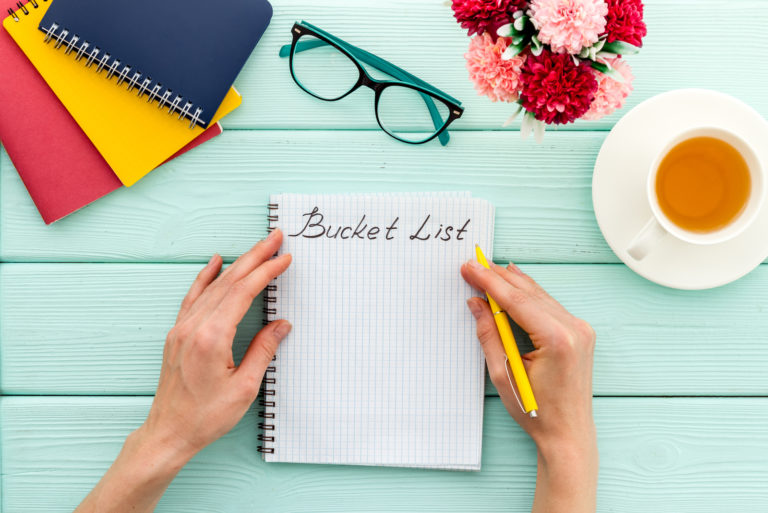 femme écrivant une liste de seaux sur la table avec des verres et du café