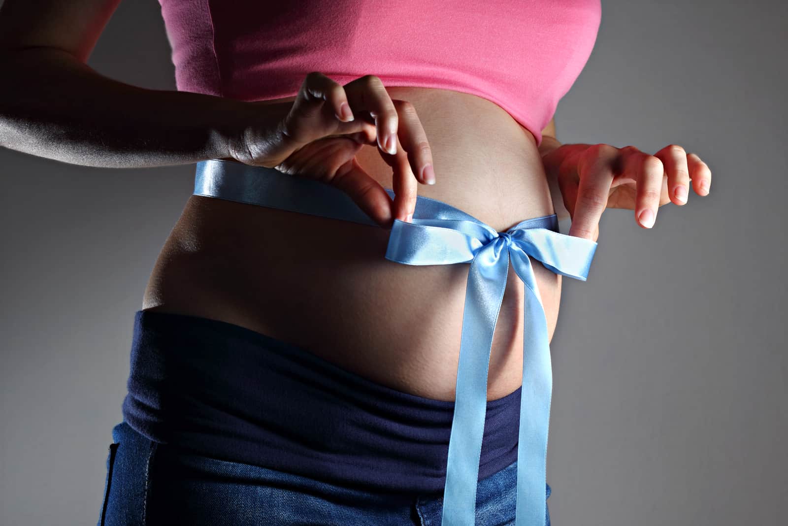 Femme enceinte tenant un ruban bleu avec un arc noué sur son ventre