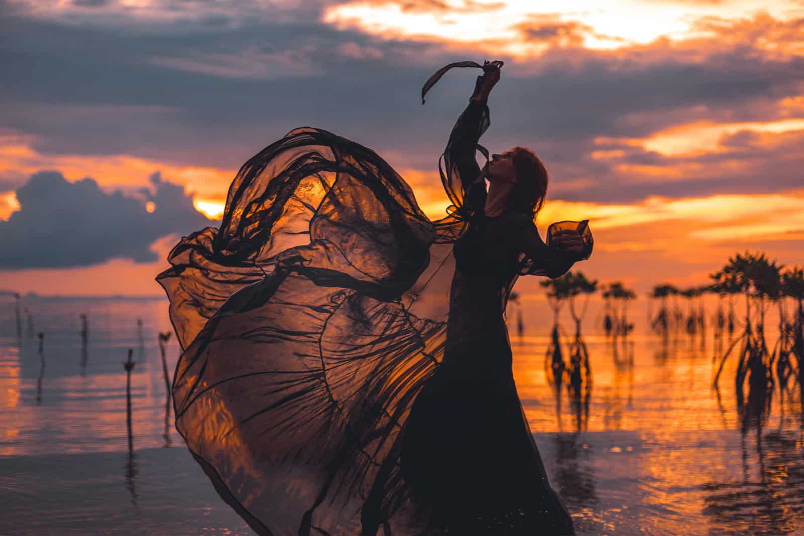 belle jeune femme dansant dans l'eau à la silhouette du coucher du soleil