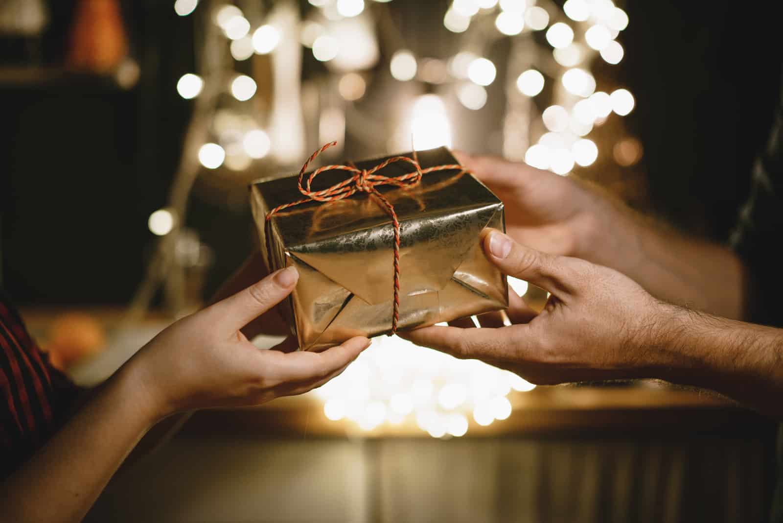 couple échangeant des cadeaux avec des guirlandes lumineuses en arrière-plan