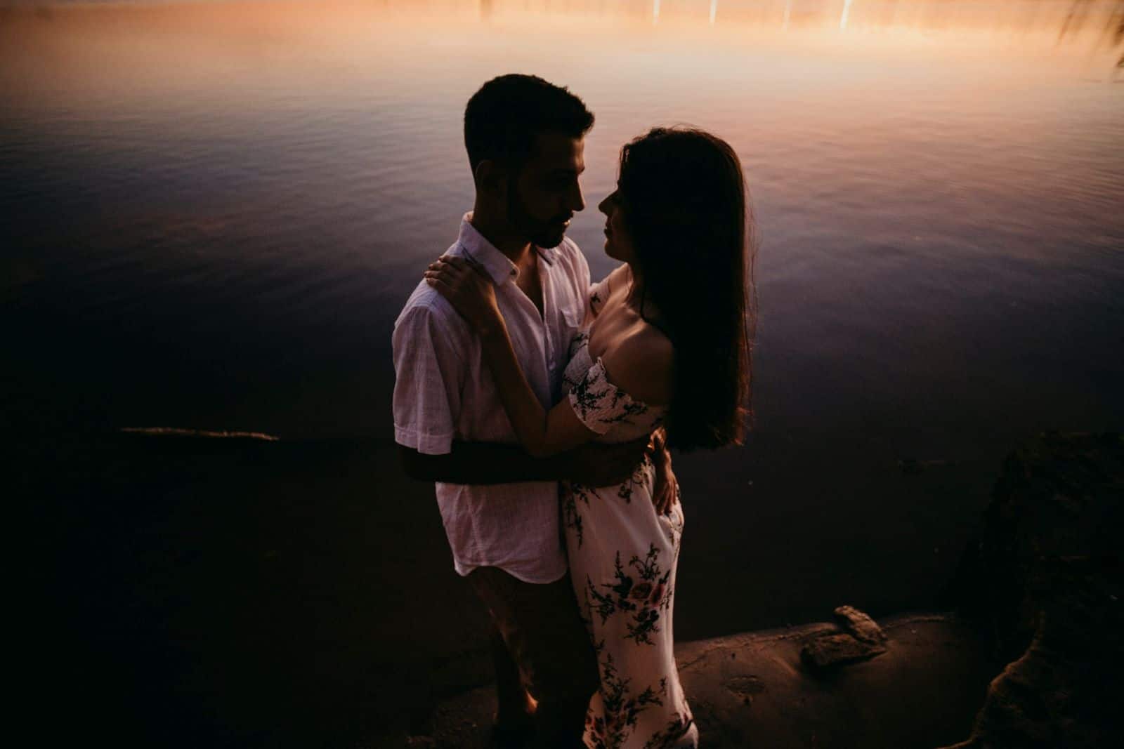 couple posant devant l'eau au coucher du soleil