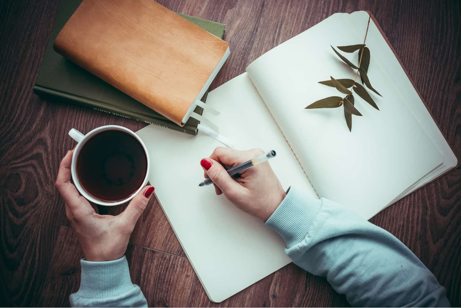 femme écrivant dans un cahier avec du café dans l'autre main