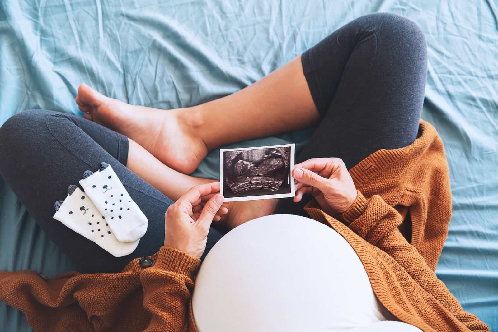 femme enceinte regardant des chaussettes de bébé et une échographie