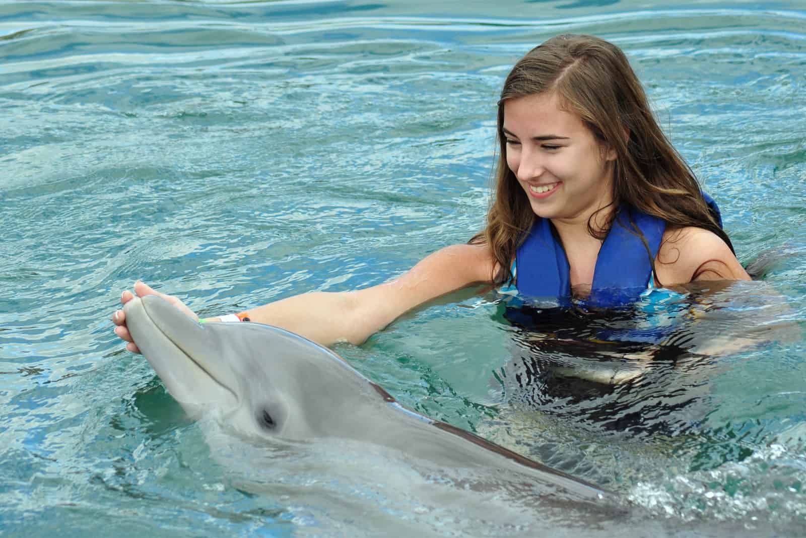 femme souriante caressant un dauphin dans la piscine