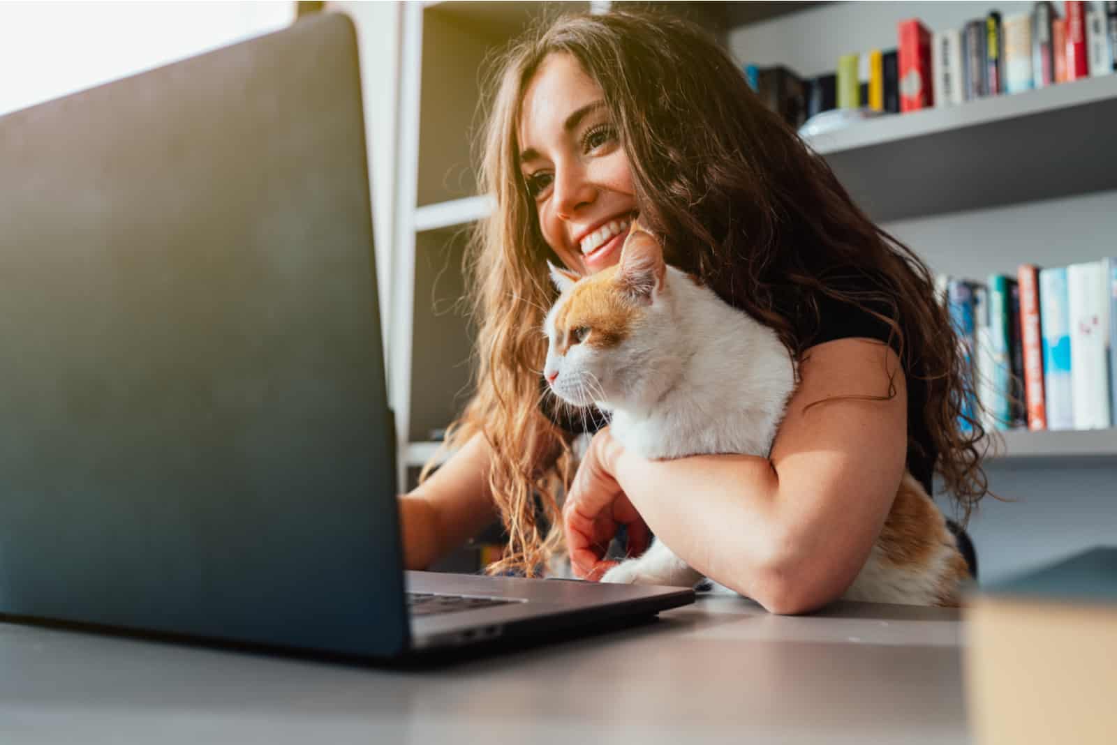femme tenant son chat et travaillant sur un ordinateur portable