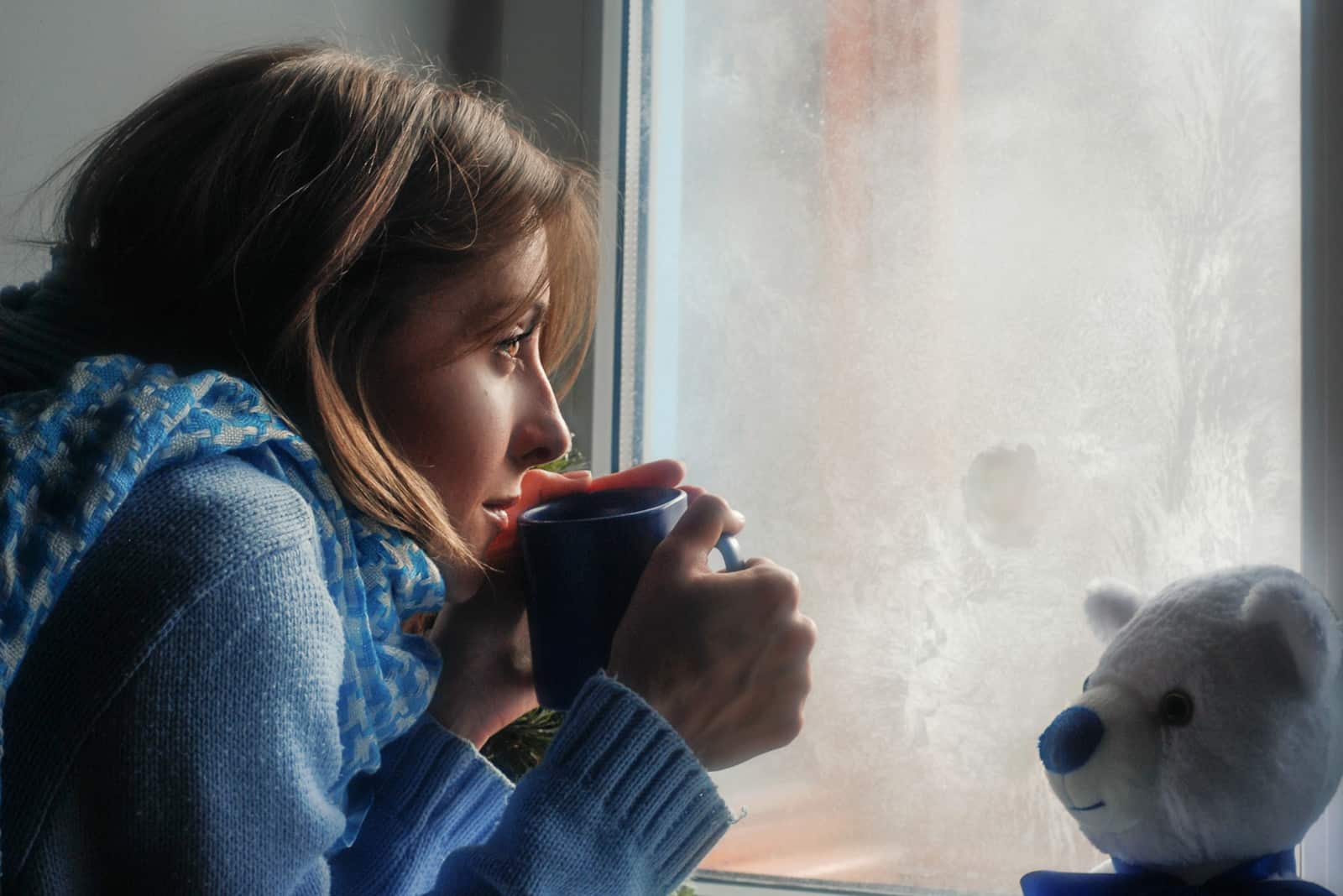 fille solitaire tenant une tasse de thé regardant par la fenêtre