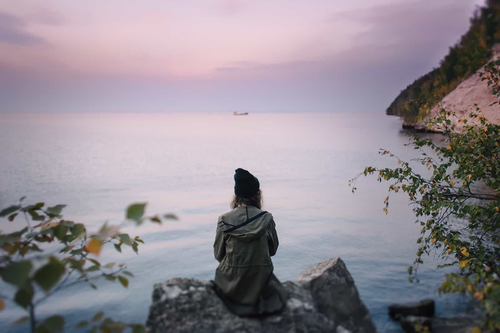 femme assise sur un rocher regardant la mer