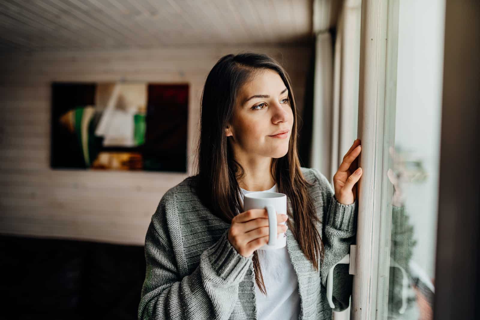 femme boit du thé et regarde par la fenêtre