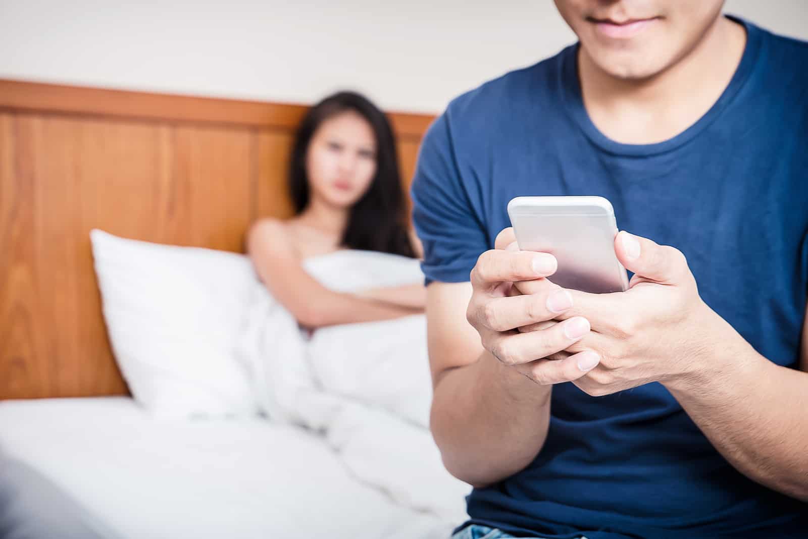 femme inquiète au lit regardant l'homme envoyer des SMS