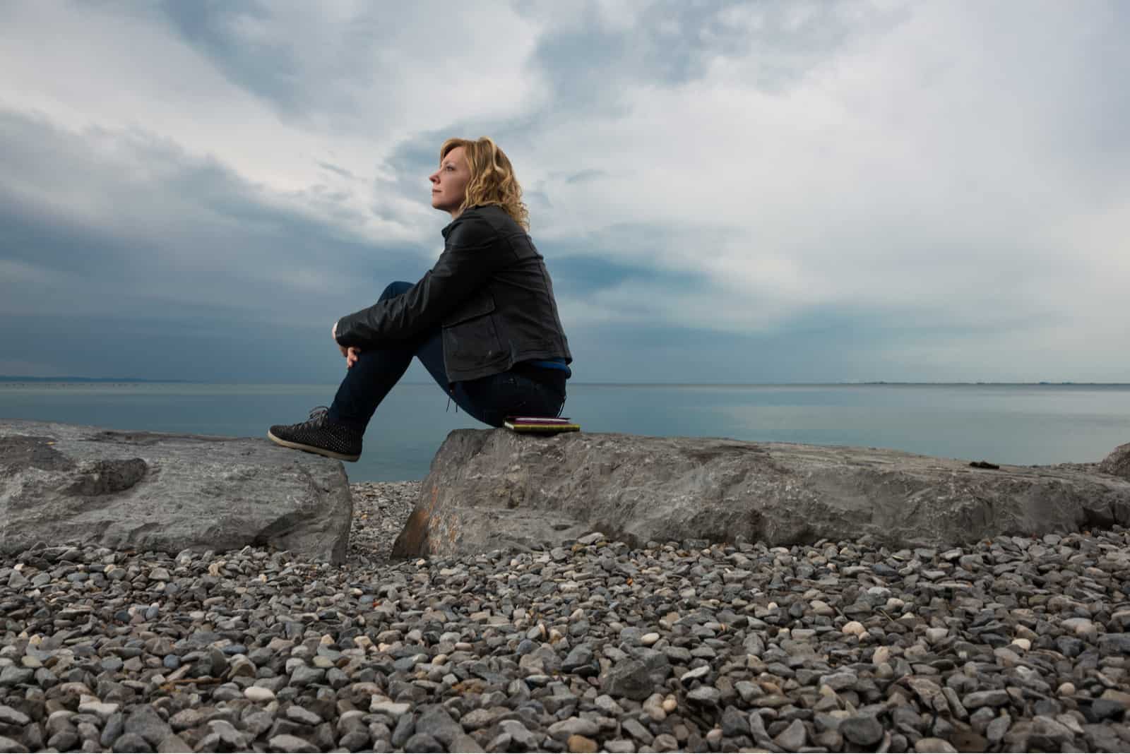femme réfléchie assise sur un rocher regardant la mer