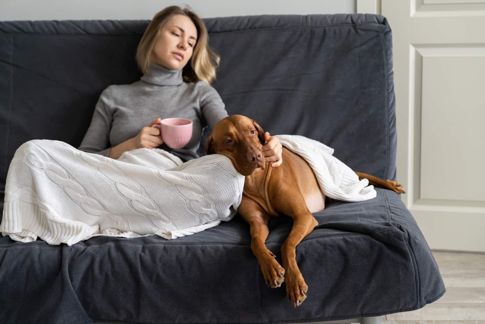 femme triste assise sur un canapé avec son chien sous une couverture
