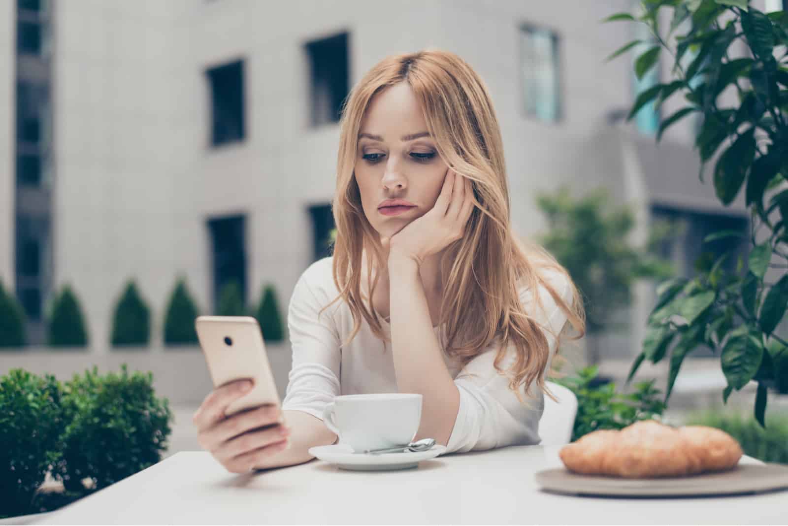 jeune femme ennuyée assise dans un café sur son téléphone