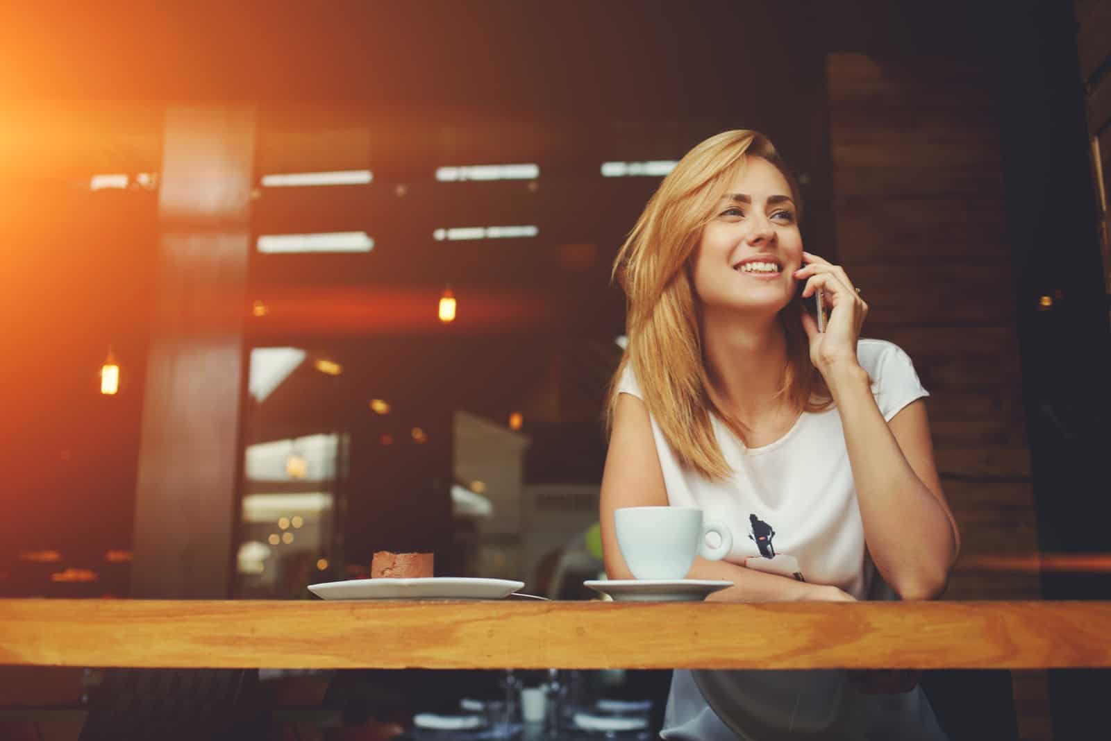 une femme souriante assise dans un café et parlant au téléphone