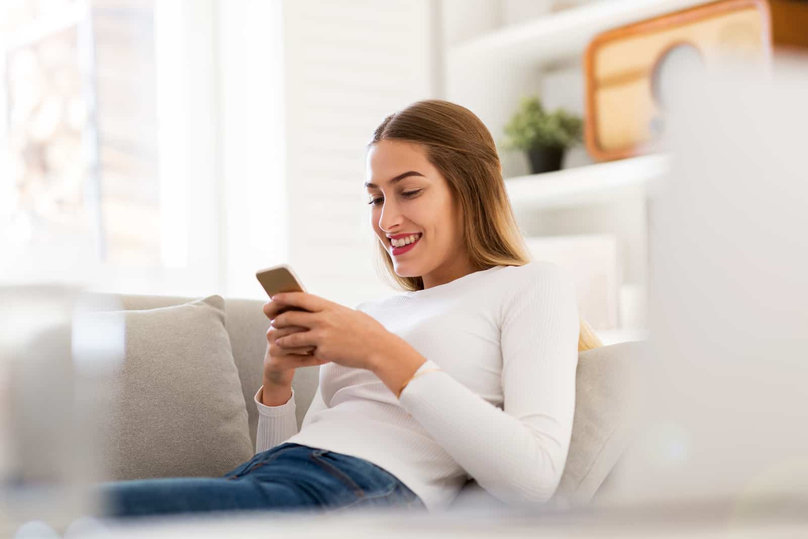 femme heureuse envoyant des textos assise sur un canapé
