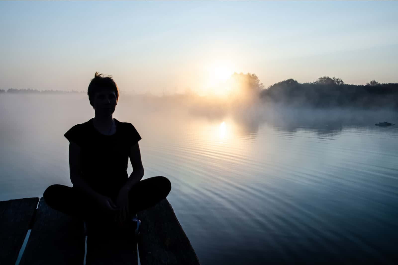 silhouette de femme assise sur un quai au bord du lac