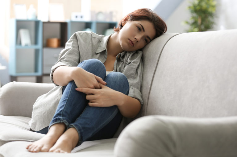 triste femme recroquevillée assise sur un canapé