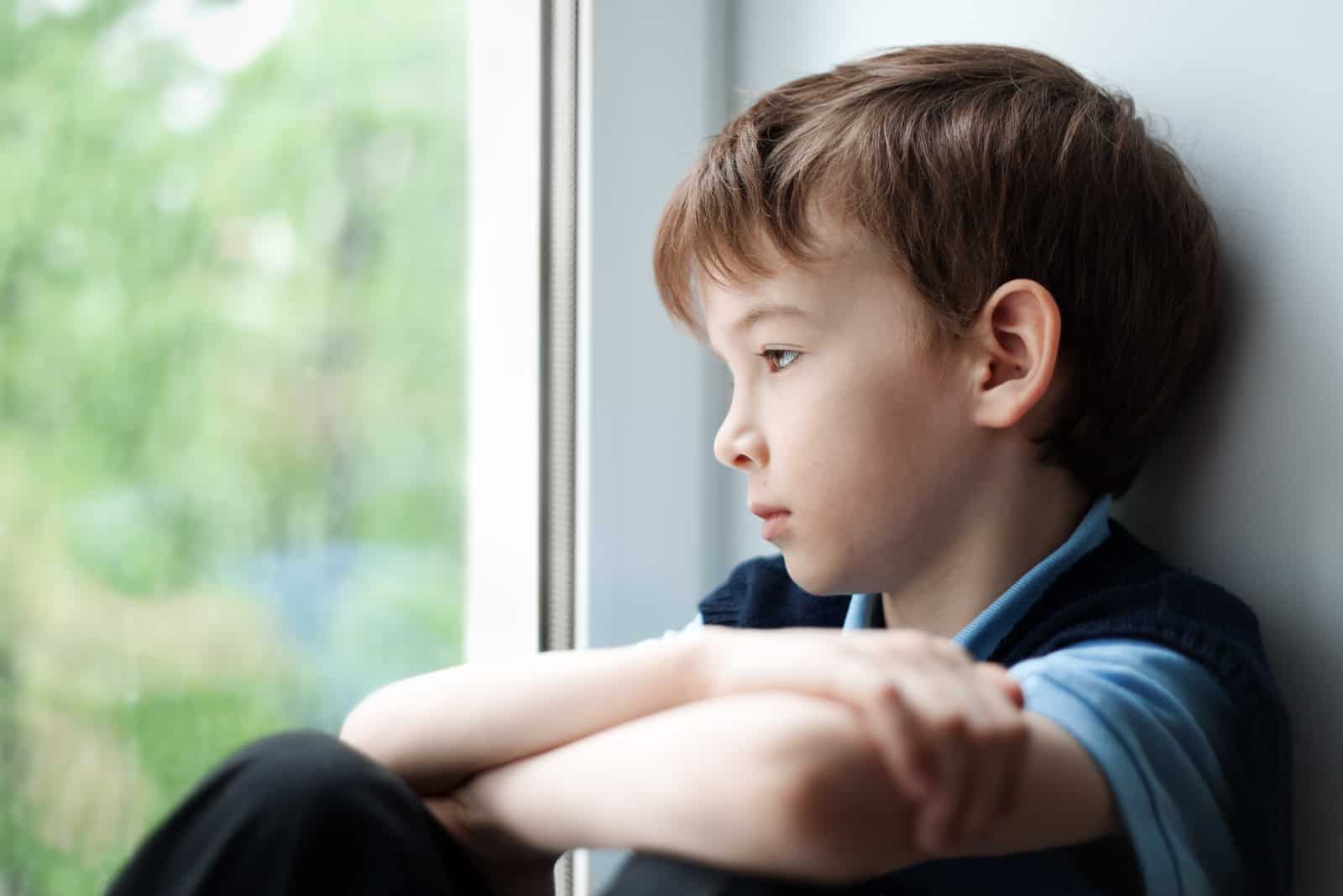 un enfant triste est assis près de la fenêtre
