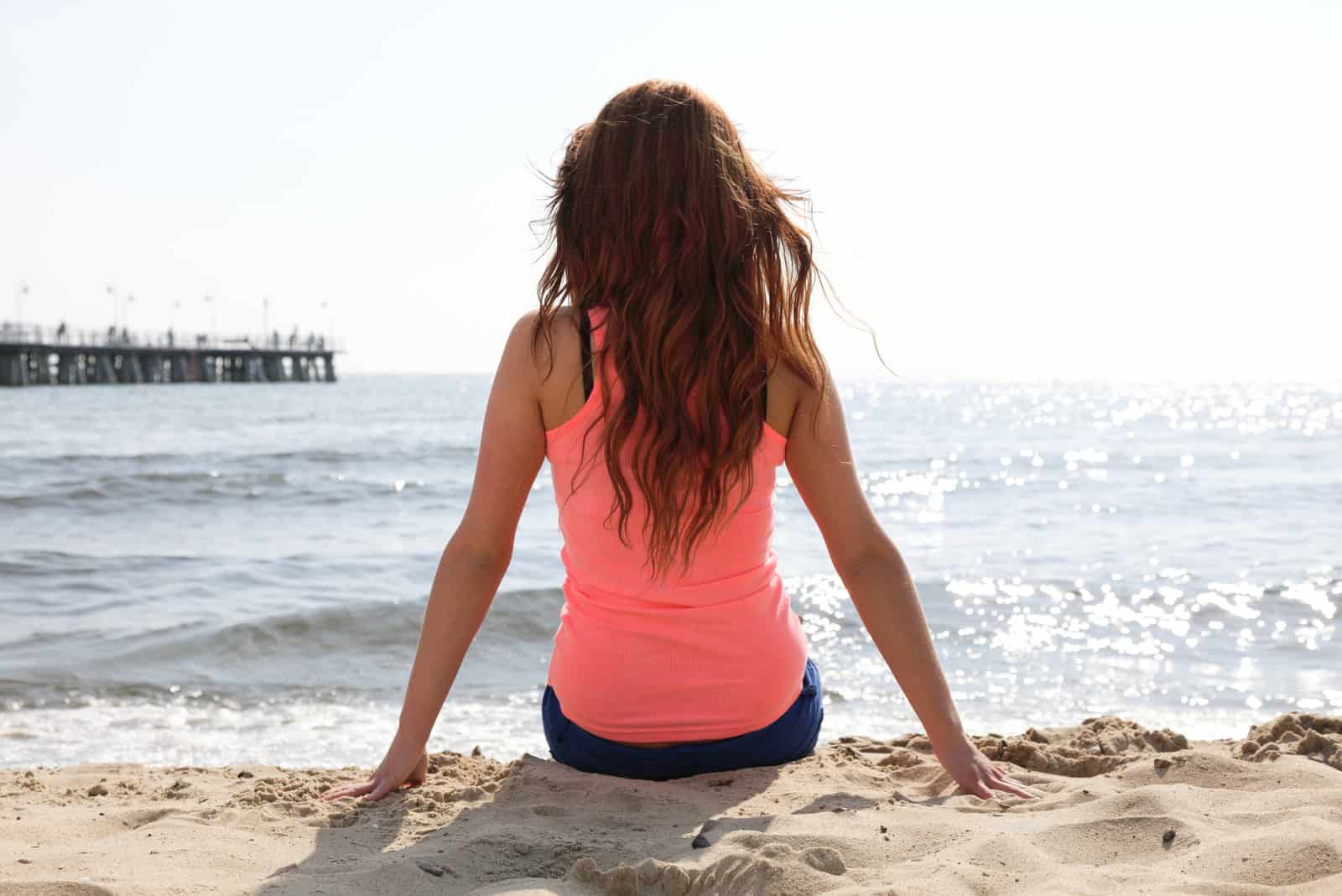 une belle femme aux longs cheveux bruns est assise sur la plage et regarde la mer