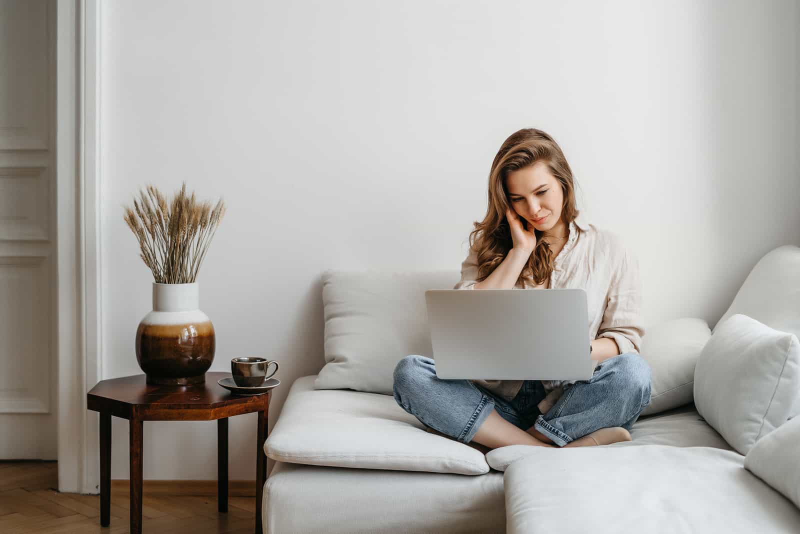 une femme aux longs cheveux bruns est assise sur le canapé et travaille derrière un ordinateur portable