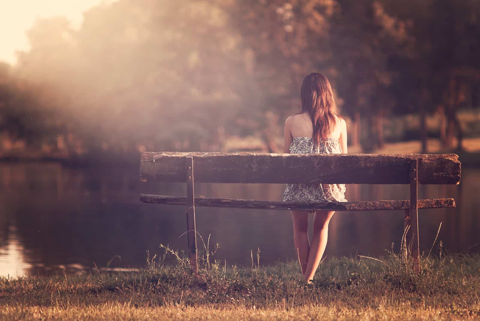 une femme aux longs cheveux bruns est assise sur un banc et regarde le lac