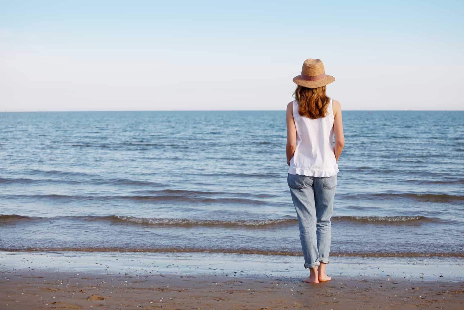 une femme avec un chapeau sur la tête marche sur la plage