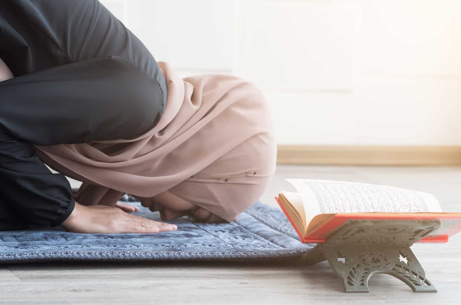 Jeune femme musulmane s'inclinant avec foi et respect sur le tapis avec coran