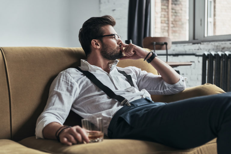 bel homme assis sur le canapé avec un verre de whisky