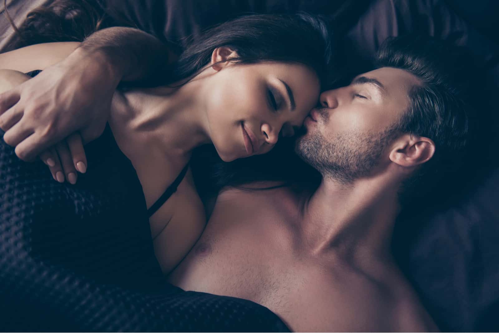un homme embrasse une femme sur le front en position couchée dans son lit