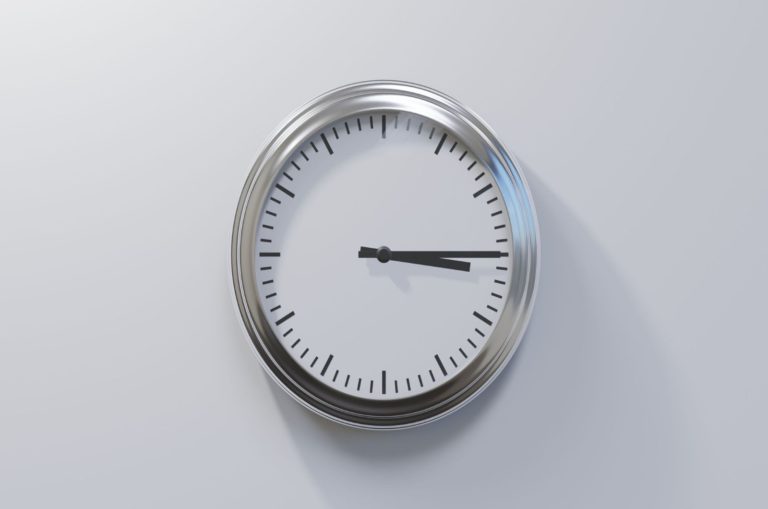 Horloge chromée brillante sur un mur blanc à trois heures et quart