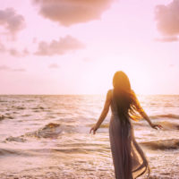 coucher de soleil d'une femme en robe blanche à côté d'une mer agitée