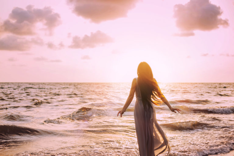 coucher de soleil d'une femme en robe blanche à côté d'une mer agitée