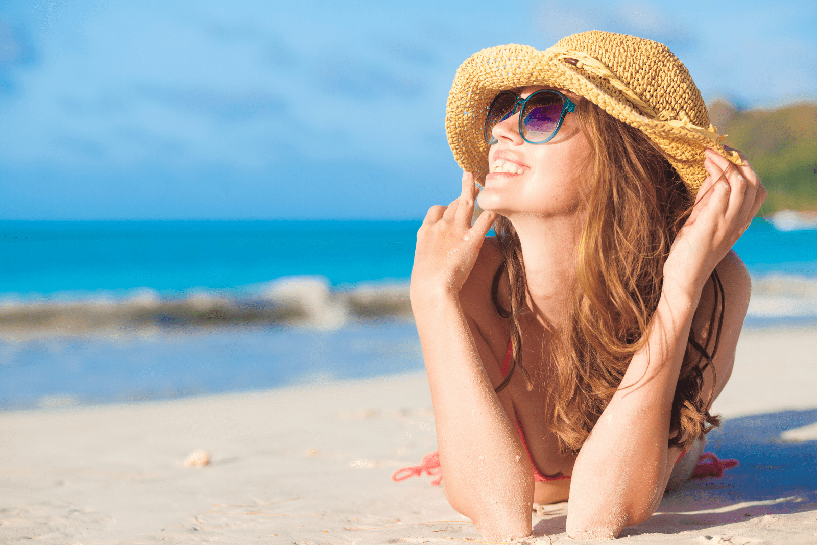 une femme souriante avec un chapeau sur la tête se trouve sur la plage