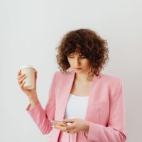 une femme est debout en train de boire du café et de taper au téléphone