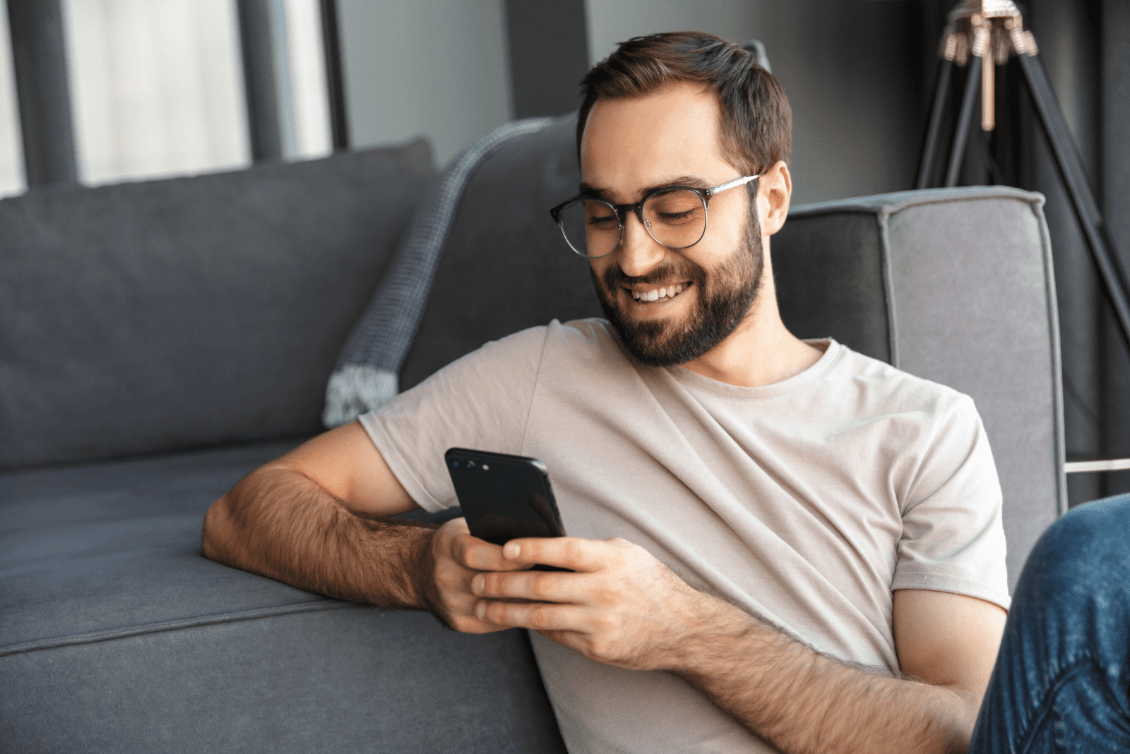 un homme souriant est assis par terre et tape au téléphone