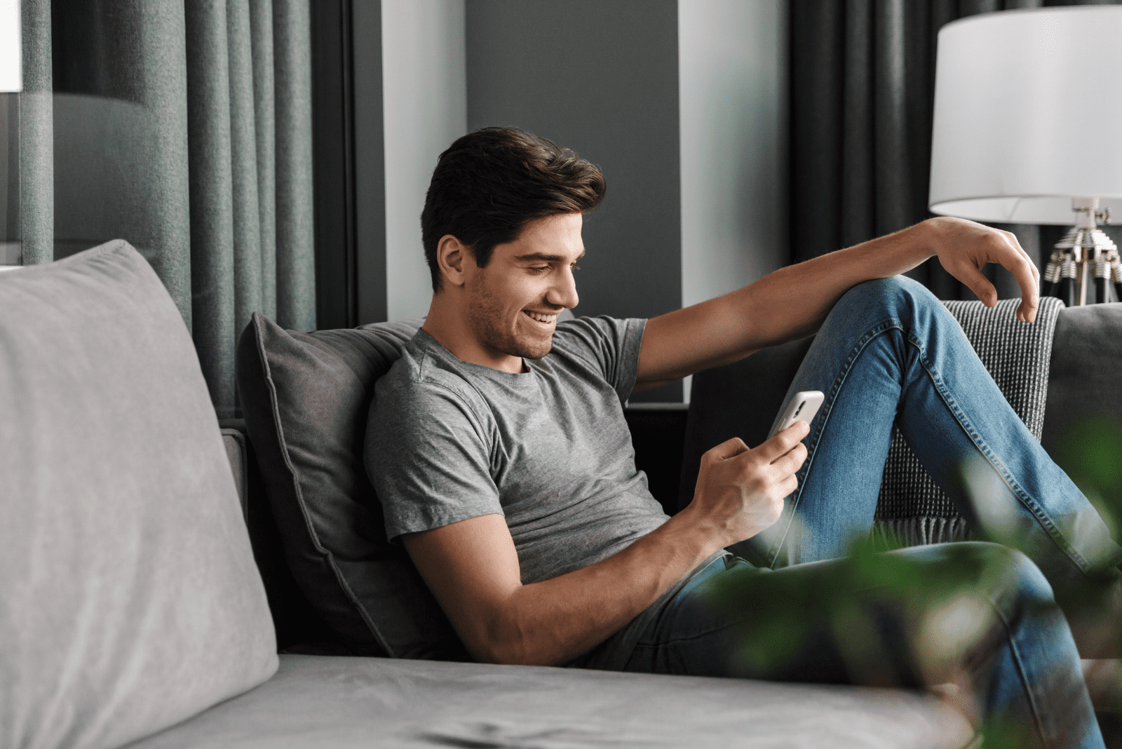 un homme souriant est assis sur le canapé et tape au téléphone