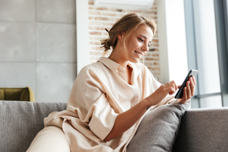 femme souriante assise sur le canapé et tapant au téléphone