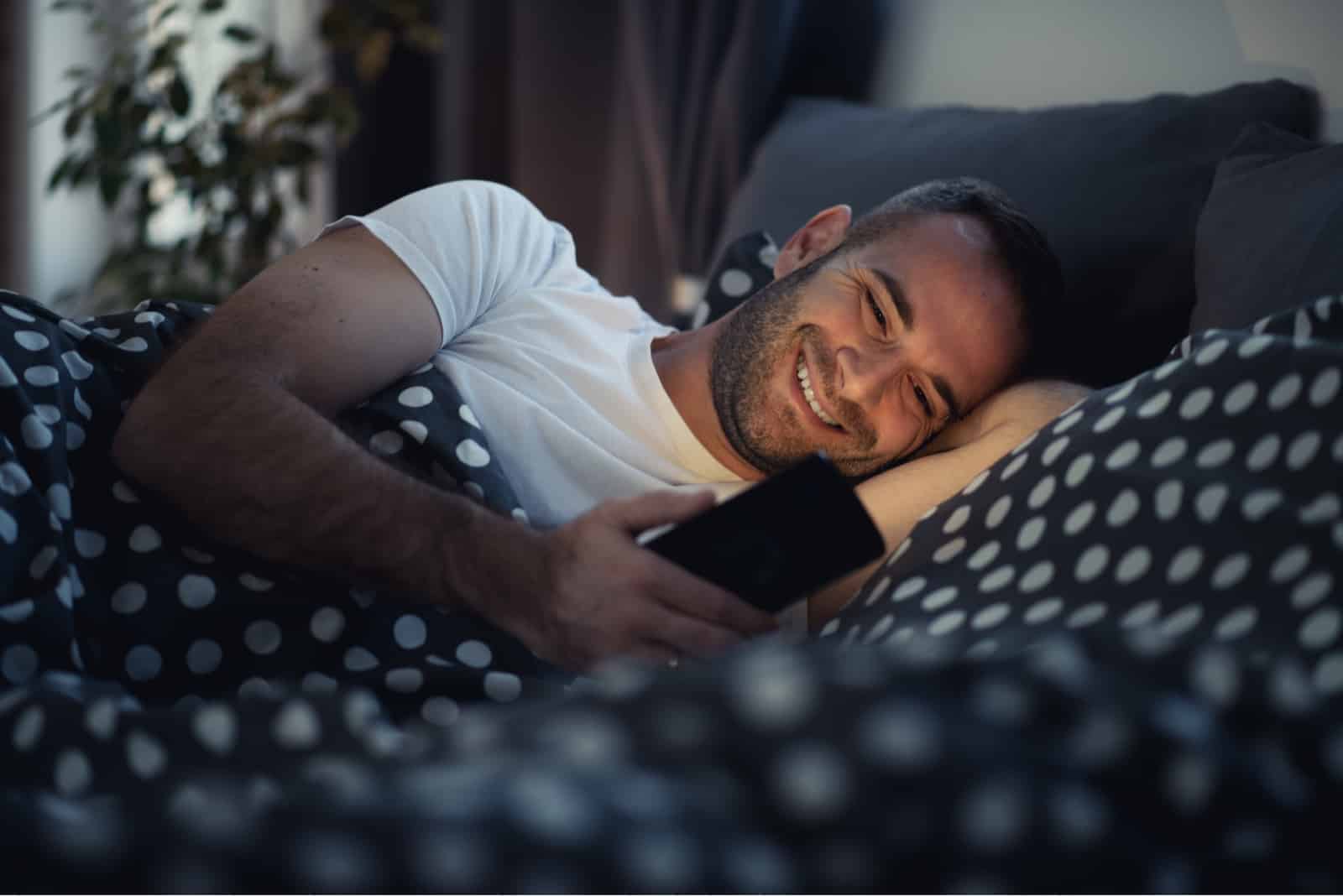 homme qui envoie des SMS en position couchée dans son lit