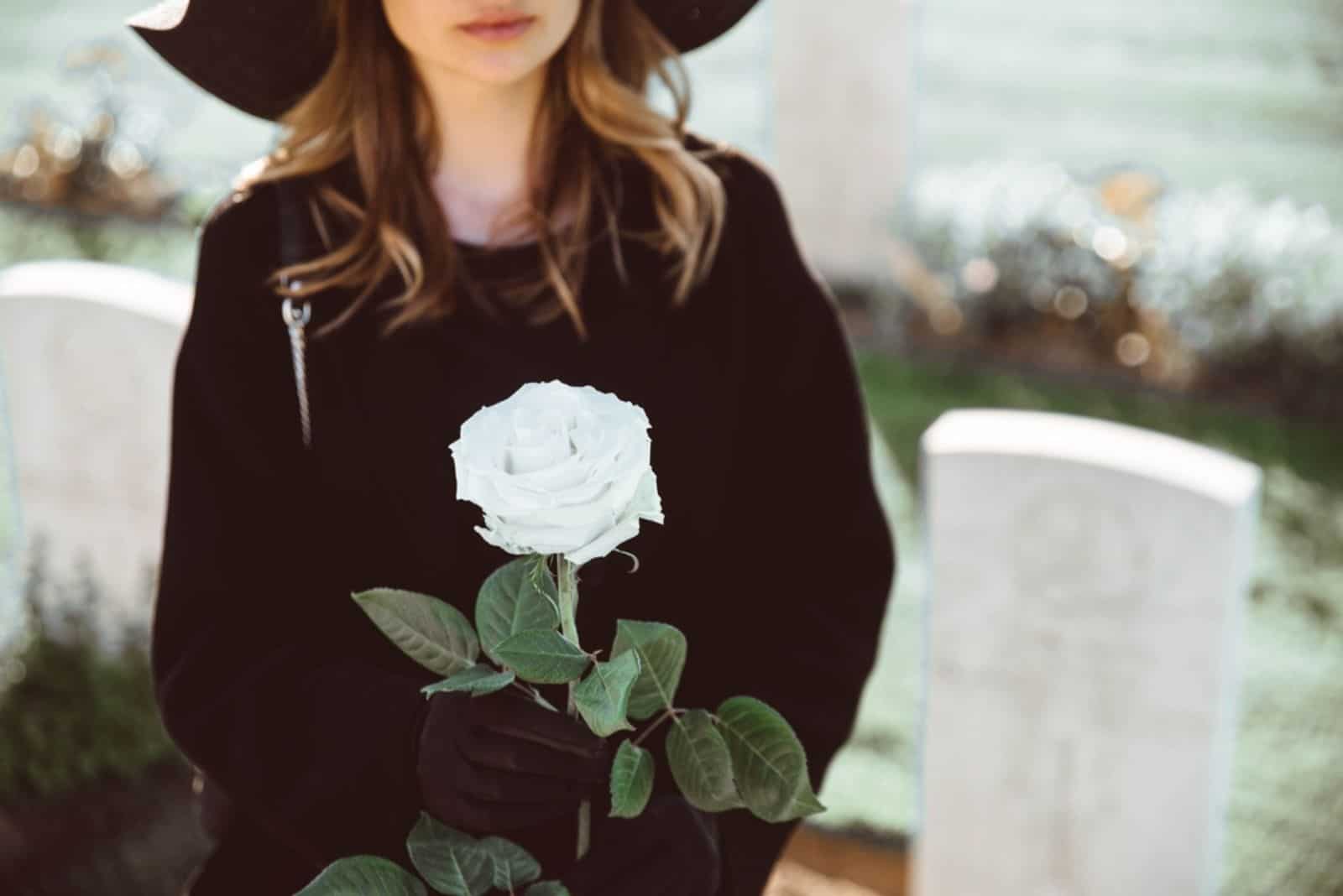 Femme triste dans le cimetière tenant un bouquet de roses à la main