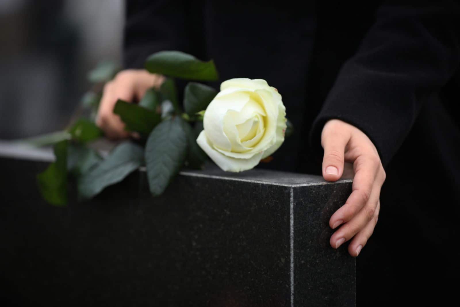Femme tenant une rose blanche près de la pierre tombale en granit noir