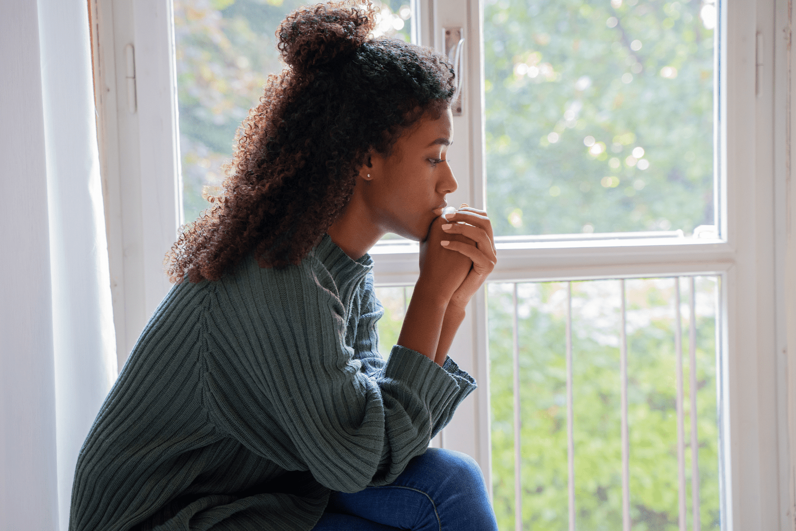 une femme est assise près de la fenêtre et prie