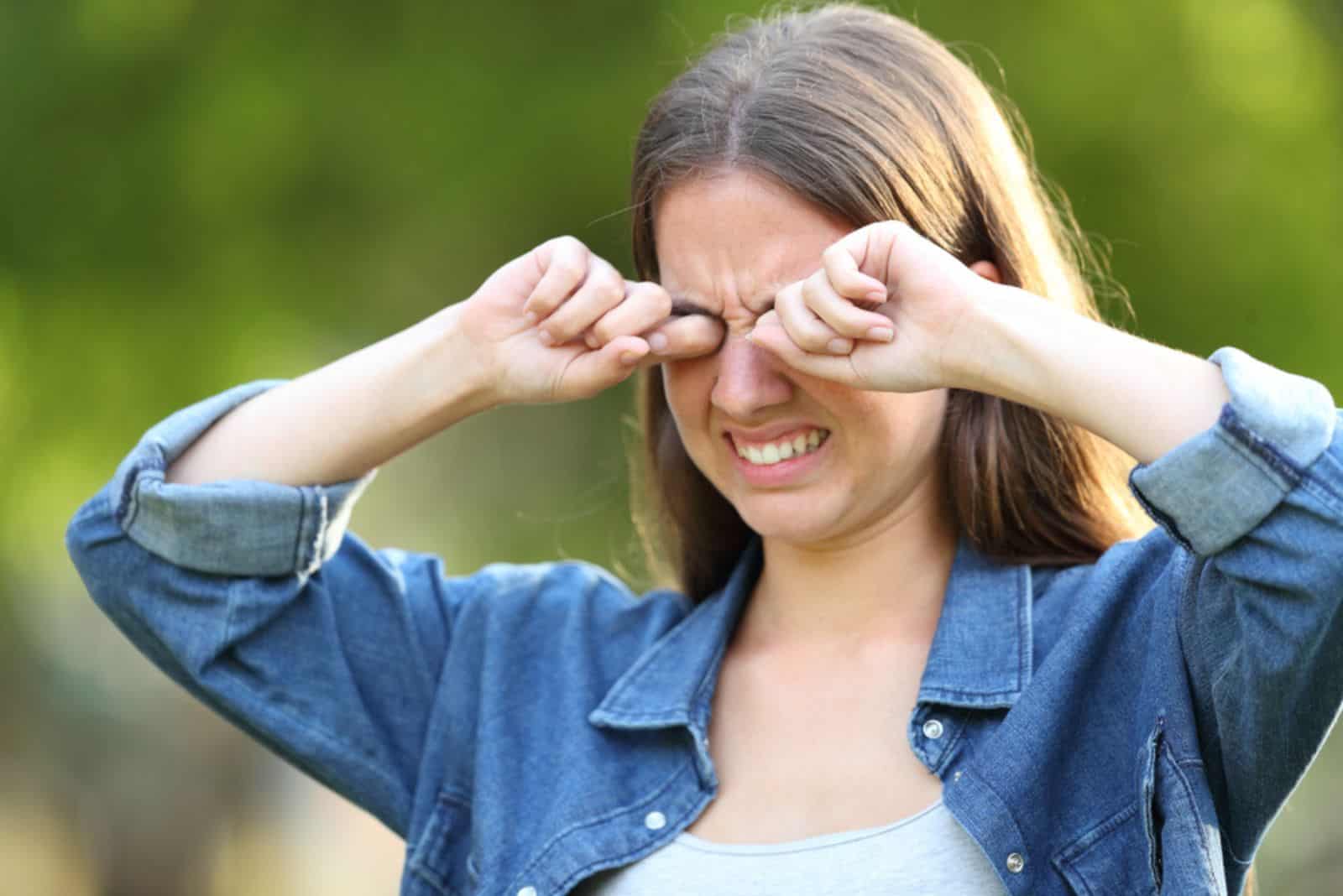 Femme souffrant de démangeaisons se gratter les yeux à l'extérieur dans un parc