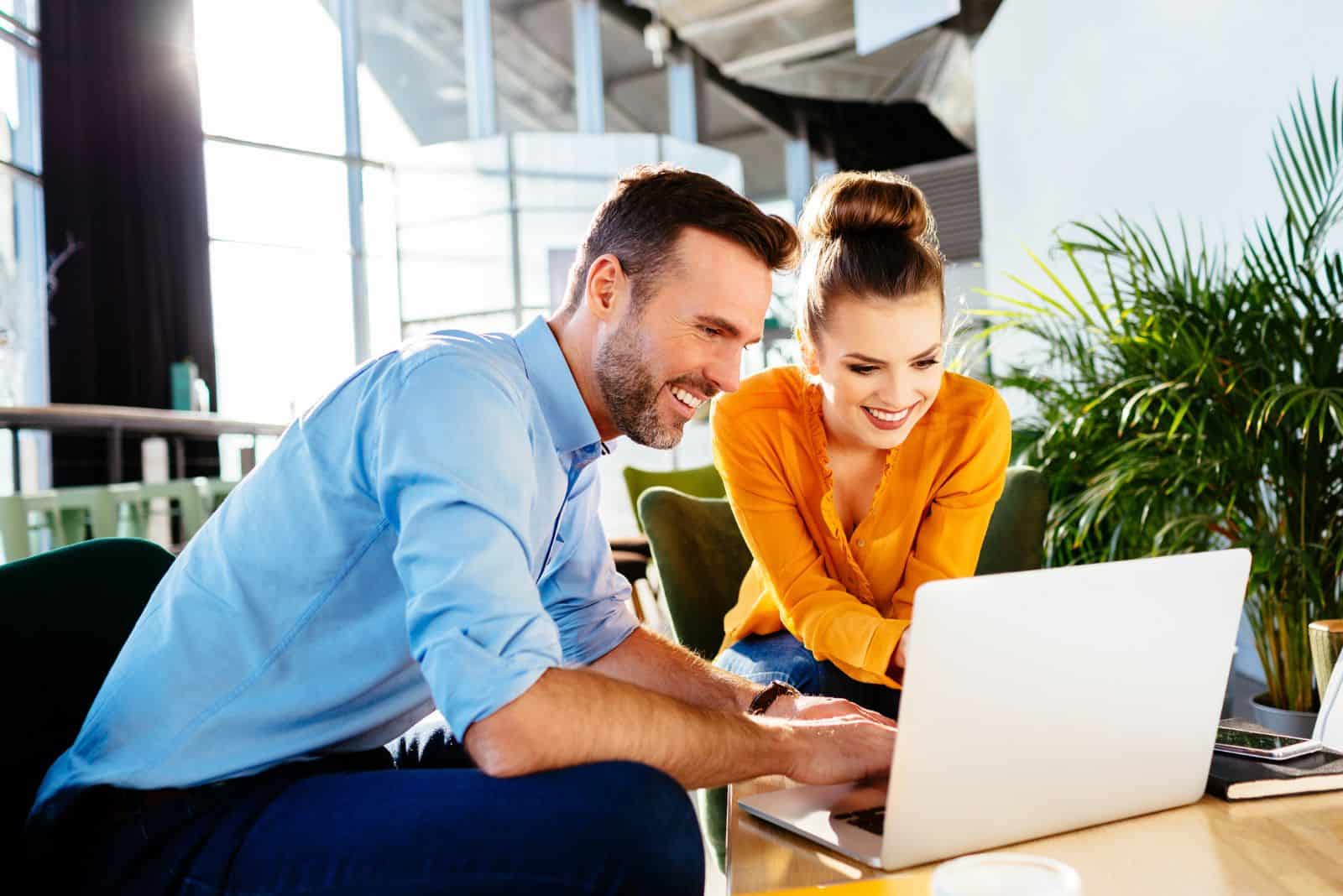 homme et femme souriants assis et regardant un ordinateur portable